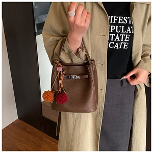 Detail of a brown lychee pattern leather bucket bag with silver lock and pompom charms