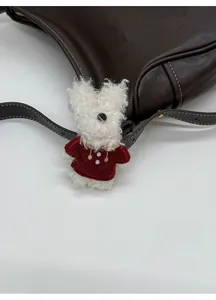 Detail of cute white plush dog charm with red sweater attached to a leather tote bag