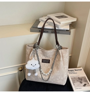 Detail of cream jacquard tote bag with floral patterns, pearl chain, and plush charm