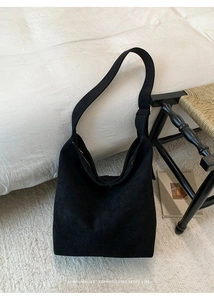 Detail of a minimalist black suede hobo bag placed on a white plush carpet in a retro setting