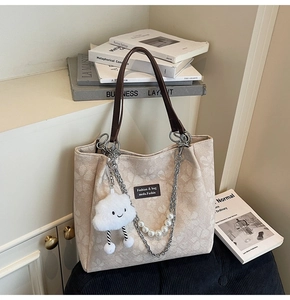 Detail of beige tote bag with floral patterns, pearl chain, and cloud charm