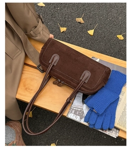 Detailed macro view of dark brown suede boston bag with dual zippers on a wooden bench