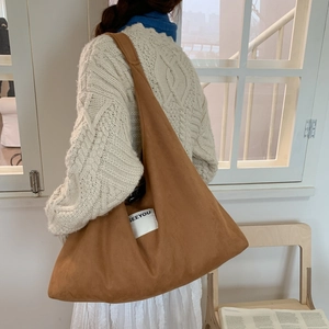 Detail of caramel suede tote bag with SEEYOU label worn over a cable knit sweater