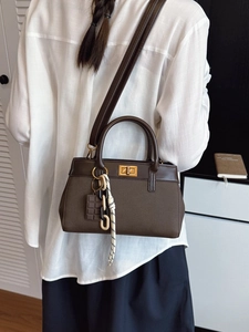 Sac seau marron foncé en cuir avec fermoir doré et breloques porté par un mannequin
