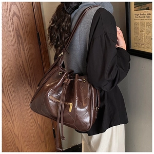 Detail of a brown quilted leather bucket bag with drawstring and metal zipper pockets