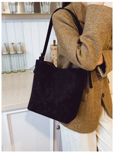 Close-up of black matte suede bucket bag with wide leather strap on model in brown tweed