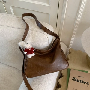 Brown leather underarm tote bag with a cute plush puppy pendant on a neutral background