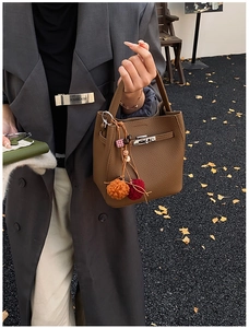 Brown lychee leather bucket bag with metal clasp and colorful pompom detail