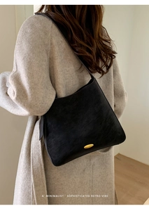 Detail of matte black leather underarm bag featuring a golden oval metal buckle on side