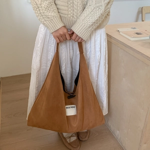 Detail of brown faux suede tote bag featuring a white SEEYOU tag and toggle button closure