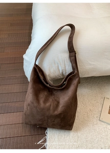 Brown suede hobo shoulder bag shown on a white bed with a minimalist retro vibe
