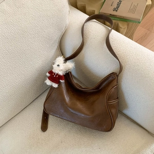 Close-up of retro brown oil-wax leather hobo bag with cute puppy plush charm on sofa