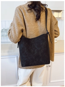 Close-up of black matte leather bucket bag worn with a brown blazer and white pants
