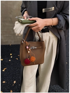 Close-up of brown pebbled leather bucket bag with lock detail and colorful charms