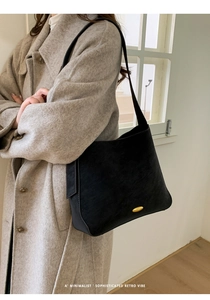 Close-up of a black retro bucket bag with a gold metal buckle on a beige wool coat