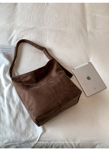 Detail of dark brown frosted suede shoulder bag with adjustable strap on beige linen background