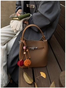 Detailed view of a brown pebbled leather bucket bag with a colorful pom-pom bag charm