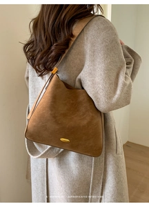 Detail view of brown vintage suede bucket bag with gold metal plaque on gray wool coat
