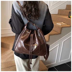 Detail of a dark brown quilted leather bucket bag with gold zipper and drawstring closure