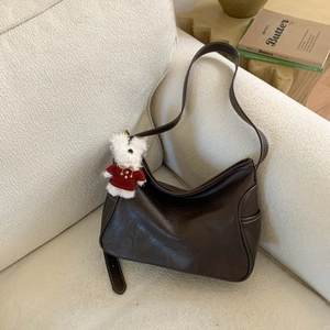 Detail of dark brown crescent bag with contrast stitching and small plush bear charm