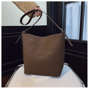 Detailed view of dark brown bucket bag with wide shoulder strap and matte leather texture