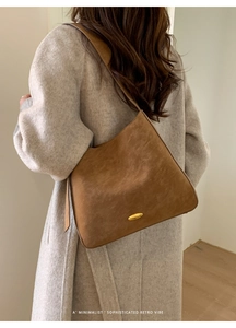 Detail of matte brown hobo bag featuring a decorative gold-tone oval metal buckle