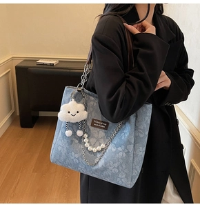 Detail of blue floral tote bag featuring pearl chain and plush cloud charm accessory