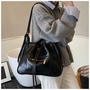 Lifestyle shot of black quilted leather drawstring bucket bag on a model's shoulder