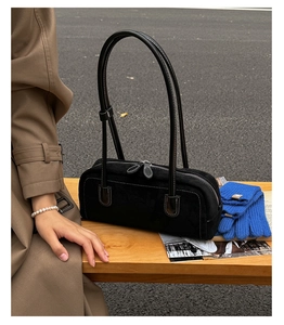 Close-up of black suede Boston bag with white stitching on a wooden bench outdoors
