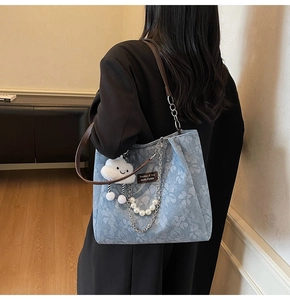 Detail view of light blue floral denim tote with pearl and cloud charms on brown leather strap
