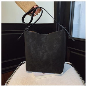 Close-up of black matte bucket bag with adjustable shoulder strap on a modern chair