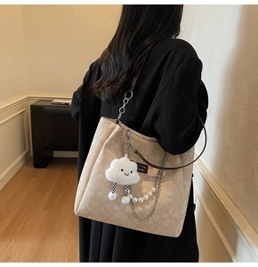 Detail of beige tote bag featuring floral texture, pearl chain, and cloud charm