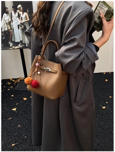 Brown lychee leather bucket bag with metal lock and plush charms on a street style model