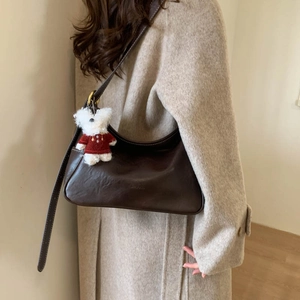 Detail of dark brown hobo bag with leather texture and cute plush bear charm accessory