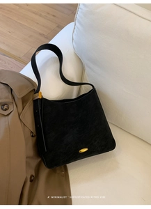 Detail of matte black minimalist bucket bag with gold metallic clasp on white sofa