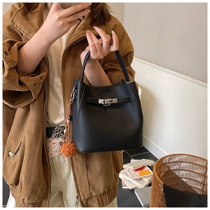 Detail of black pebbled leather bucket bag with silver turn-lock and orange pompom charm