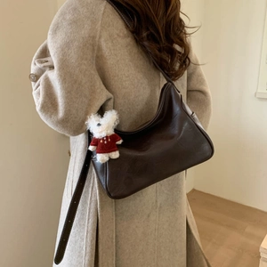 Close-up of a retro brown shoulder bag featuring a cute white teddy bear plush charm