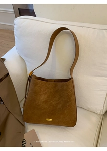 Detail of vintage brown bucket bag with oval metal accent on white sofa