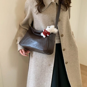Detail shot of a brown matte leather hobo crossbody bag with a plush bear charm on coat
