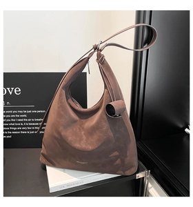 Detail of a brown Hobo bag with knotted shoulder strap and embossed brand logo on white books