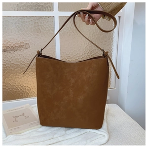 Close-up of large brown suede bucket bag with adjustable strap and decorative side ties