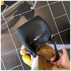 Detail of black pebbled leather bucket bag with silver clasp and orange pompom charm