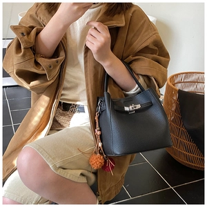 Detail of black lychee leather bucket bag with silver turn-lock and colorful pompom charms