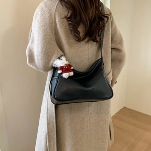 Detail of black matte leather crescent bag with white bear pendant and stitching on shoulder strap