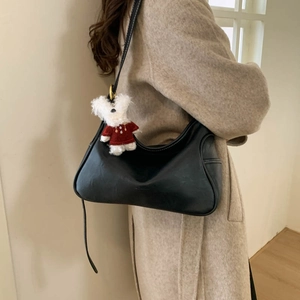 Detail of black crescent shoulder bag with cute white plush puppy charm on a model