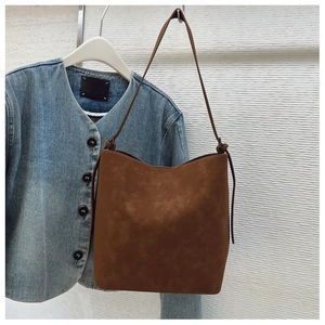 Detailed view of brown bucket bag in matte finish with knotted strap on a denim backdrop