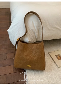 Close-up of brown textured leather bucket bag featuring gold metal hardware and wide strap