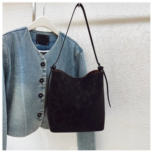 Detail of a black suede bucket bag with slim shoulder strap and spacious open top design