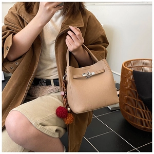 Detail of apricot pebbled leather bucket bag with silver turn-lock and colorful pom-poms