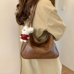 Detail view of brown vintage shoulder bag with visible stitching and plush bear charm
